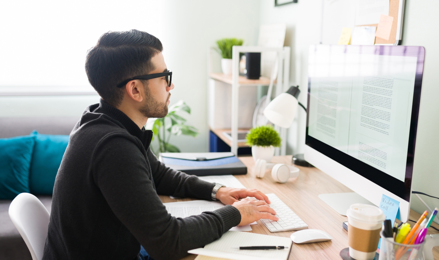 Hispanic young male writer with glasses sitting at his desk and writing his next book on the computer