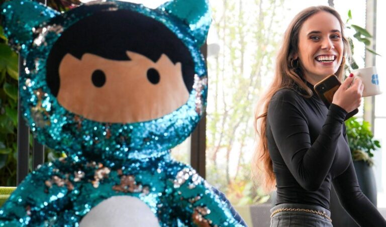 Alicia enjoying a coffee at Salesforce Dublin Tower, sitting on a green bench next to a big, blue sequined Astro plush