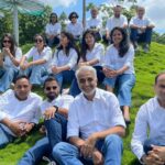 A group of Salesforce employees in matching white button down shirts and blue jeans sit on a grassy hill outside