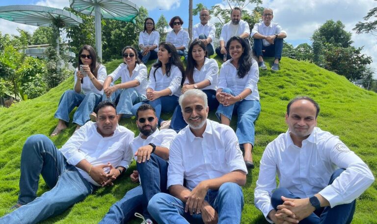 A group of Salesforce employees in matching white button down shirts and blue jeans sit on a grassy hill outside
