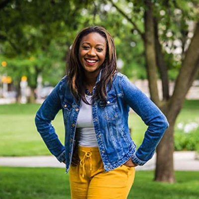 Kai Johnson in a denim jacket stands outside amidst garden paths.