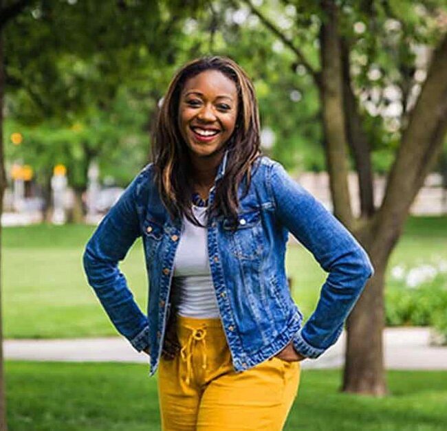 Kai Johnson in a denim jacket stands outside amidst garden paths.
