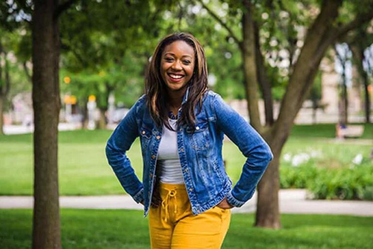 Kai Johnson in a denim jacket stands outside amidst garden paths.