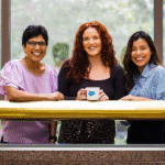 Three women, Salesforce employees smiling and are sharing some time together.