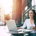 Happy beautiful young businesswoman working on laptop in street cafe outdoor